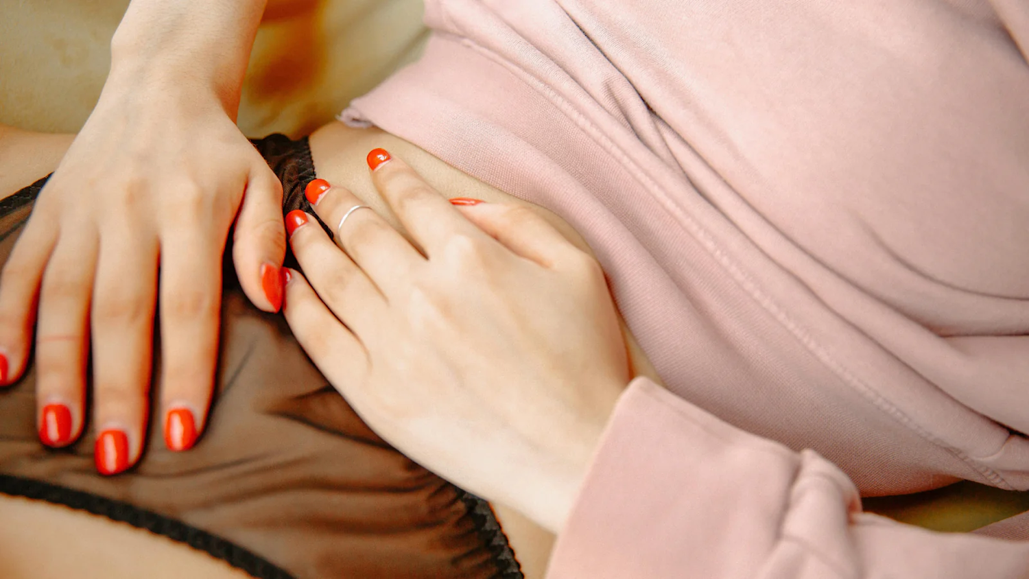 Person resting hands on lower abdomen while lying down, suggesting menstrual cramps or stomach discomfort.