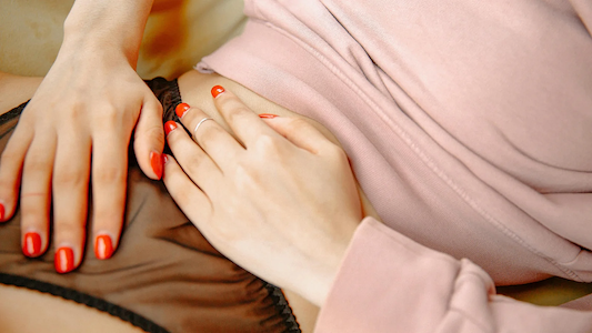 Person resting hands on lower abdomen while lying down, suggesting menstrual cramps or stomach discomfort.