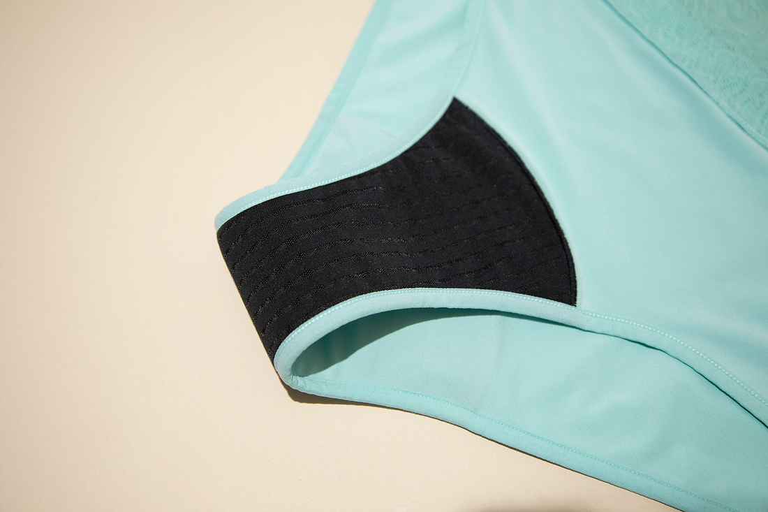 Close-up of absorbent black lining inside mint-green period underwear displayed against a light background.