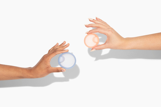 Two hands holding reusable menstrual discs against a light background with soft shadows.