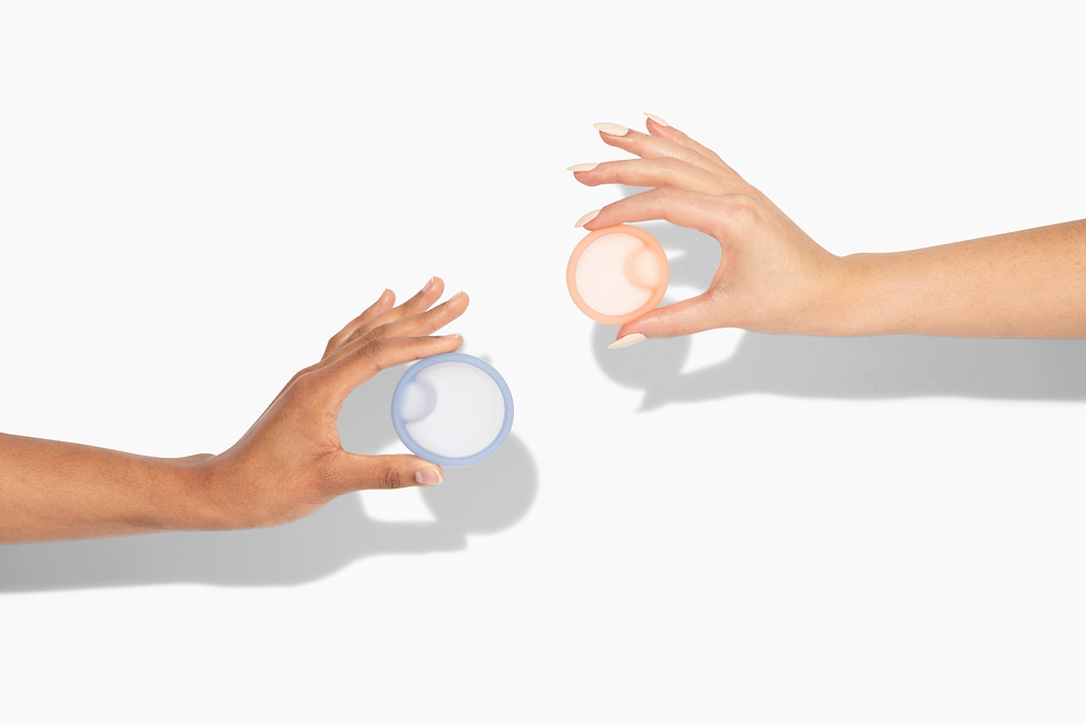 Two hands holding reusable menstrual discs against a light background with soft shadows.