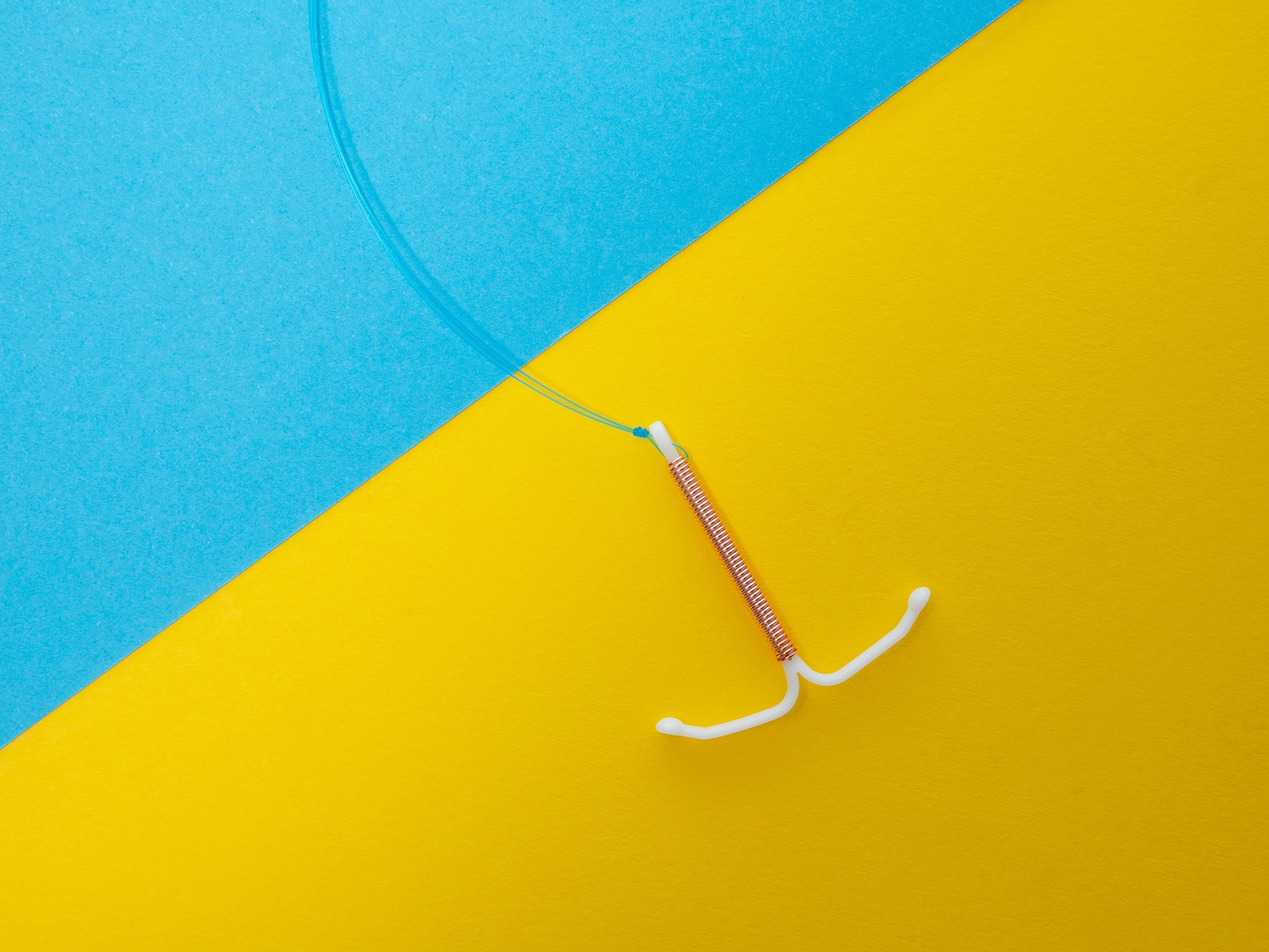 Copper IUD contraceptive device on blue and yellow background with visible removal strings
