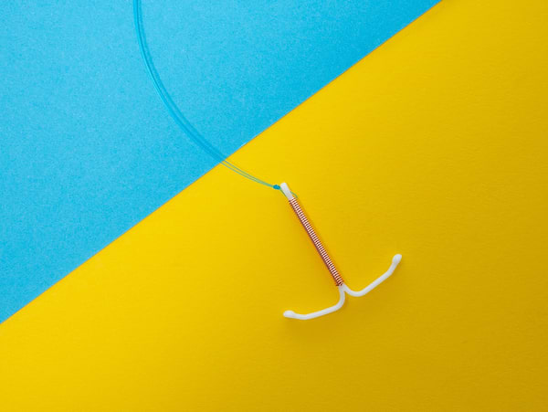 Copper IUD contraceptive device on blue and yellow background with visible removal strings