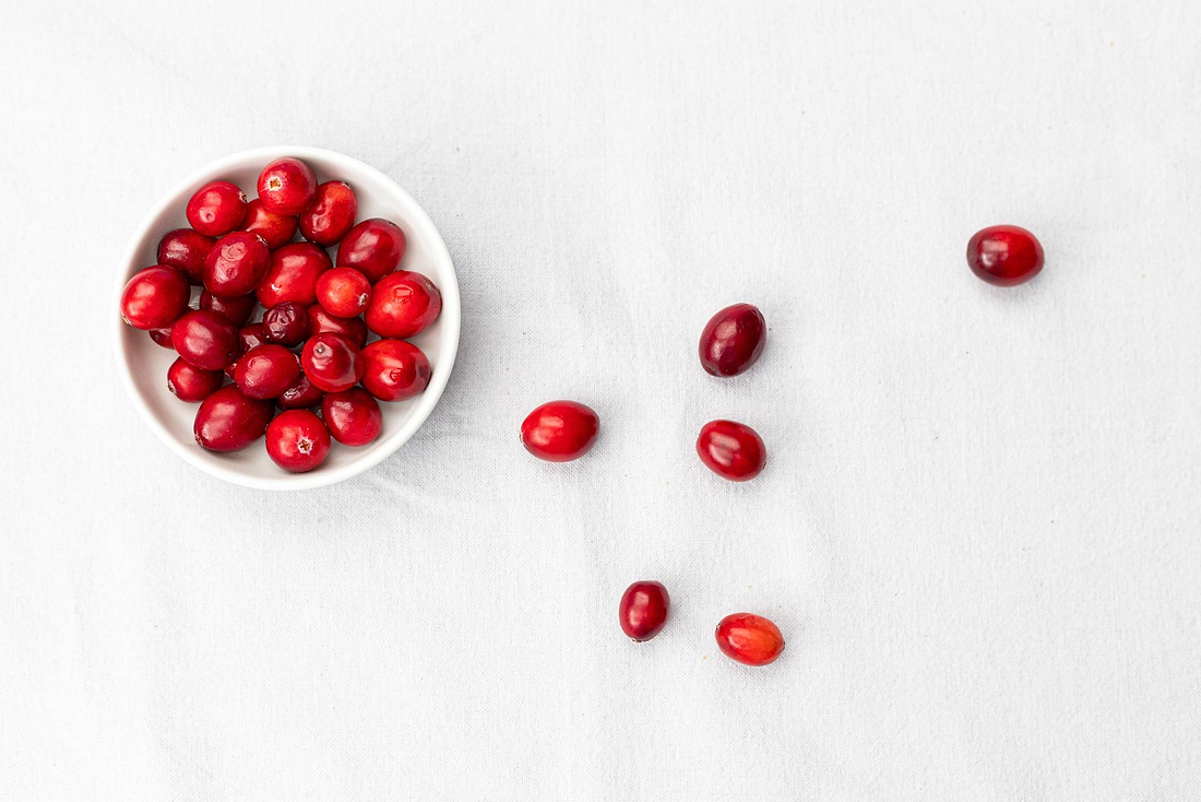 Bowl of fresh cranberries with scattered berries on a light gray fabric background