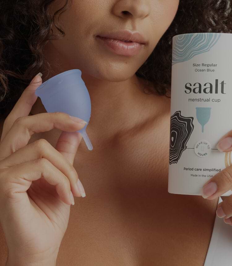 A vertical website banner for Saalt showing a person holding a blue menstrual cup and its packaging. Text overlay reads, "Painful periods? A new study links cups and discs to a user-reported decrease in menstrual cramping," followed by a "Shop Cups & Discs" button.