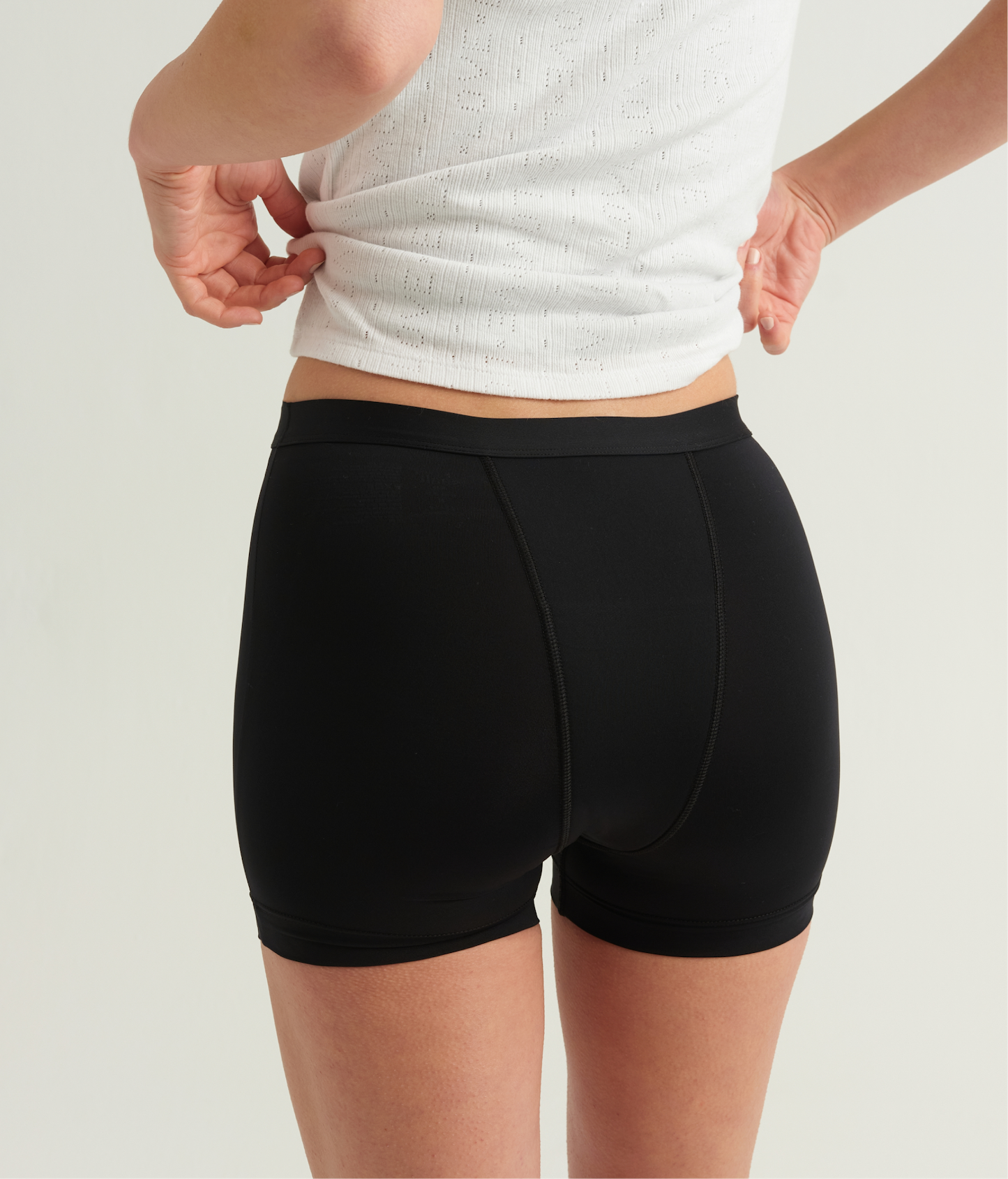 Person wearing black shorts and a white top on a light background