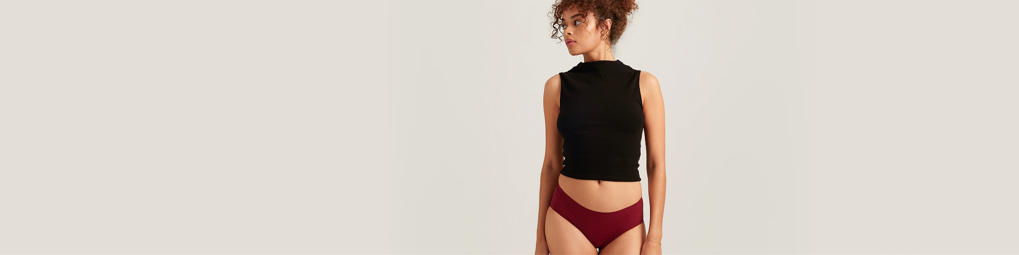 Woman wearing a black sleeveless top and maroon underwear on a beige background