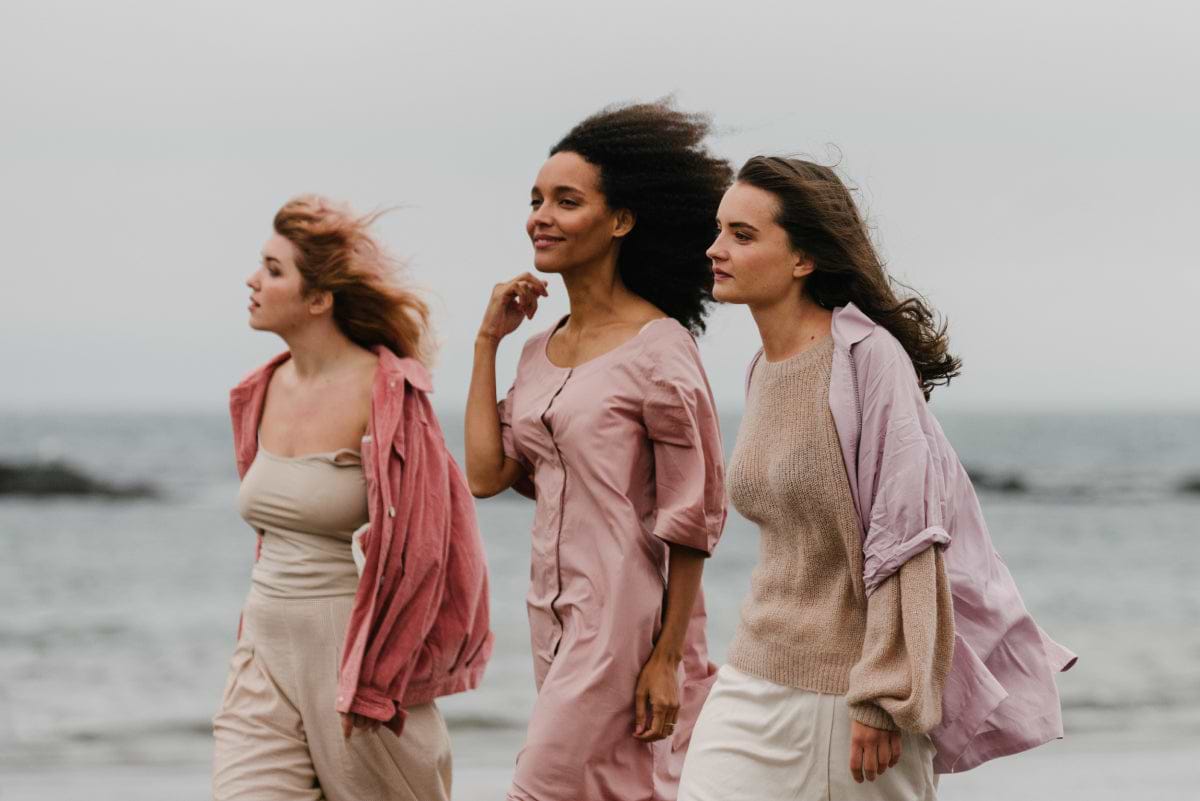 Three Females standing in front of some water with their hair blowing in the wind