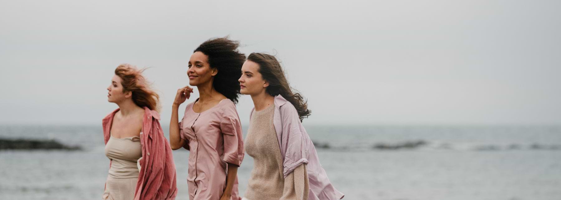 Three Females standing in front of some water with their hair blowing in the wind