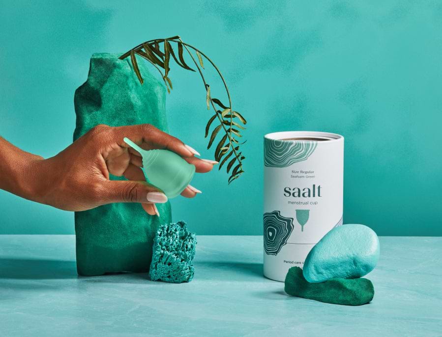 Female hand holding Saalt Menstrual Cup next to product packaging 
