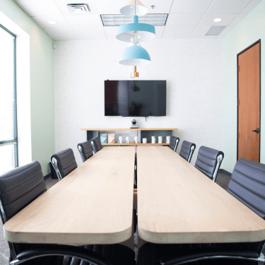 overview of meeting room with two long tables, chairs and a tv