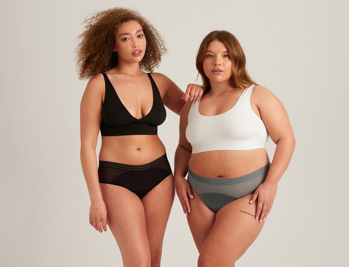 Two models wearing Saalt leakproof underwear. Model on the left is wearing the Saalt leakproof Mesh Hipster in Volcanic Black with a black bralette. Model on the right is wearing the Saalt leakproof Thong in Blue Rain with a white cropped tank.