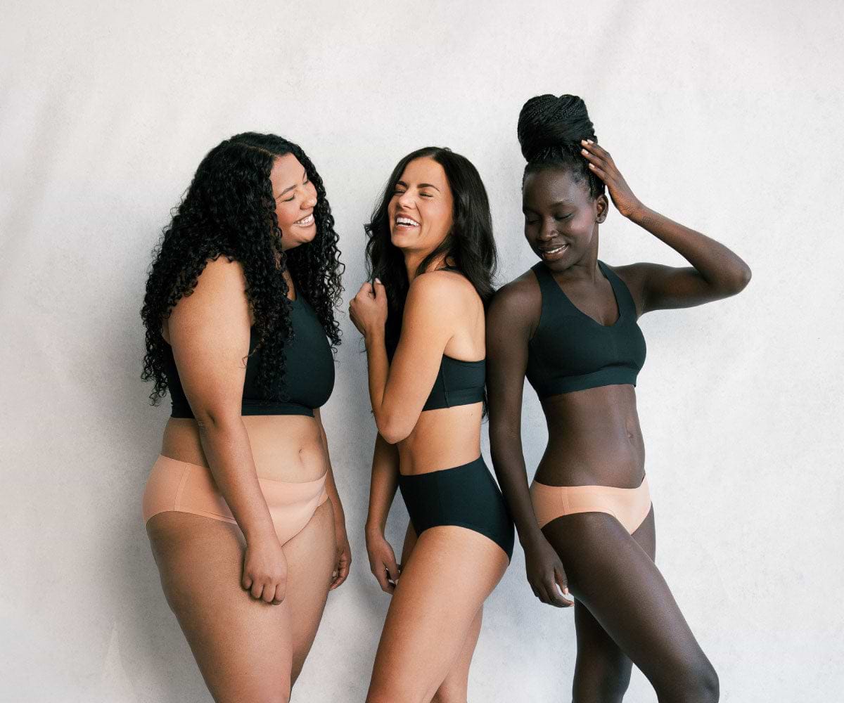 Three females wearing Saalt menstrual underwear, looking and laughing with each other