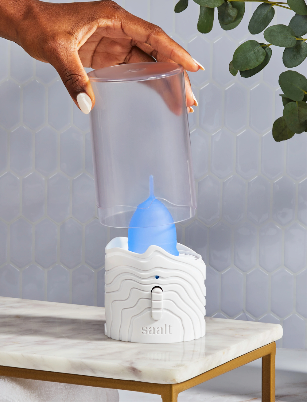 A hand lifting the lid of Saalt’s Steamer. Inside the Steamer is a Saalt Cup in color Ocean Blue. The Steamer is sitting in a marble bathroom.