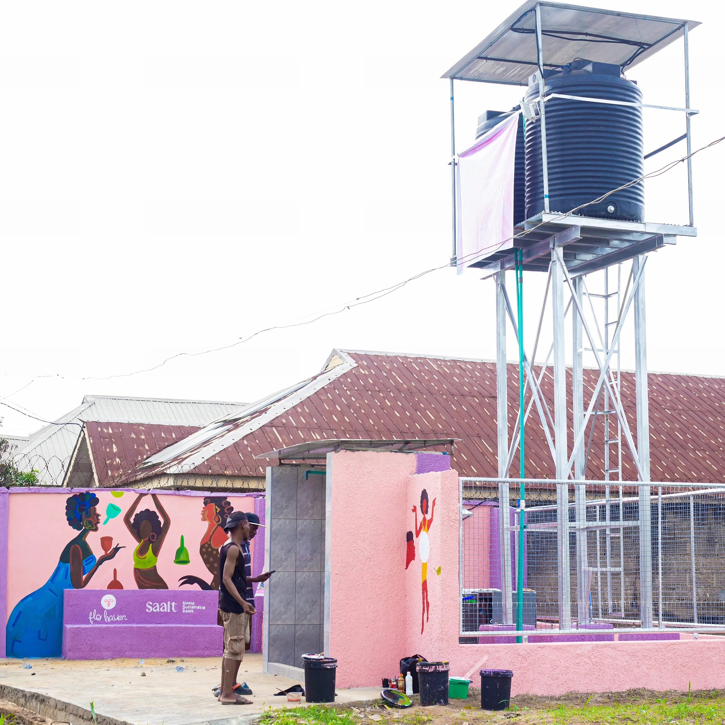 Water tower with a pink building and mural in the background