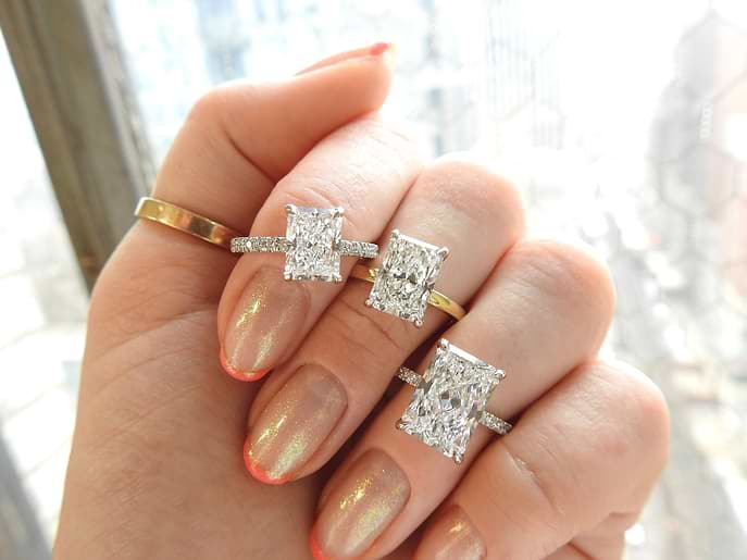 three different carat radiant cut diamond rings on a woman's hand