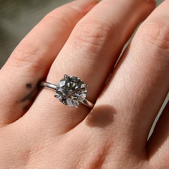 A close up shot of hand displaying a large round cut diamond solitaire on the ring finger, with sunlight highlighting the diamond's sparkle.