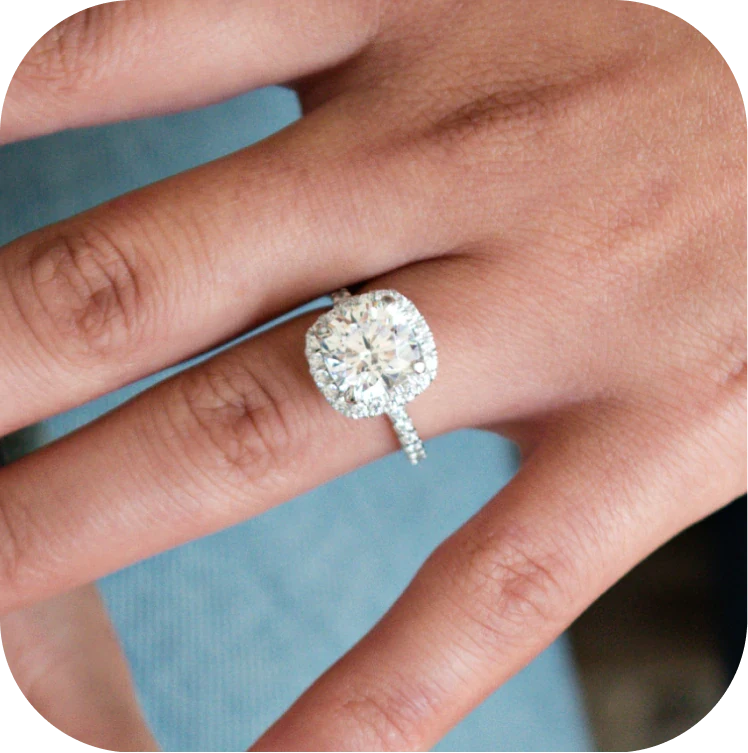 A hand wearing a square-cut diamond ring, set against a blue fabric background.