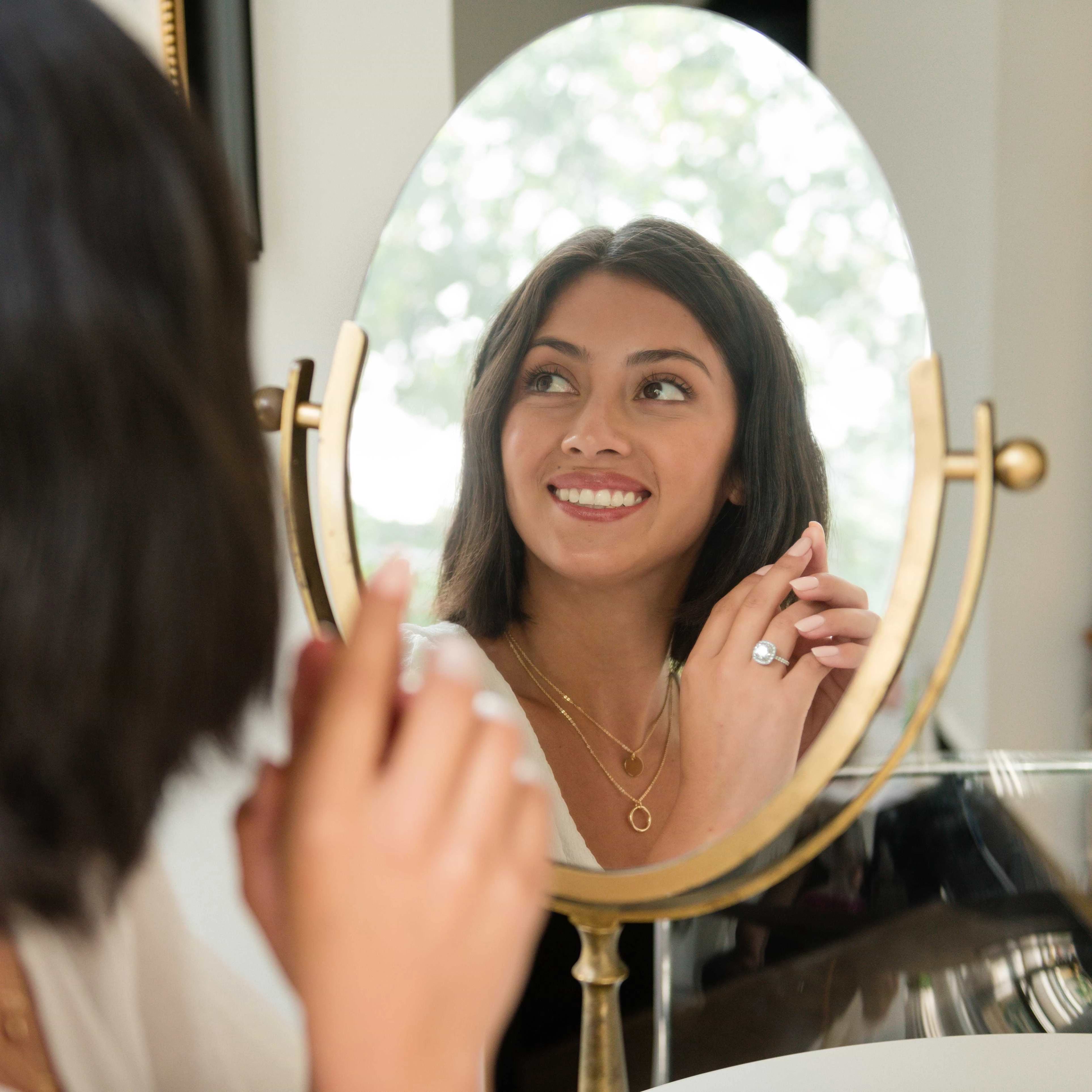 woman sitting in front of a vanity mirror holding up her lab grown diamond engagement ring