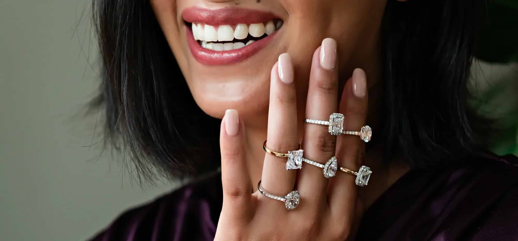  woman smiling with a hand up to face displaying multiple diamond rings
