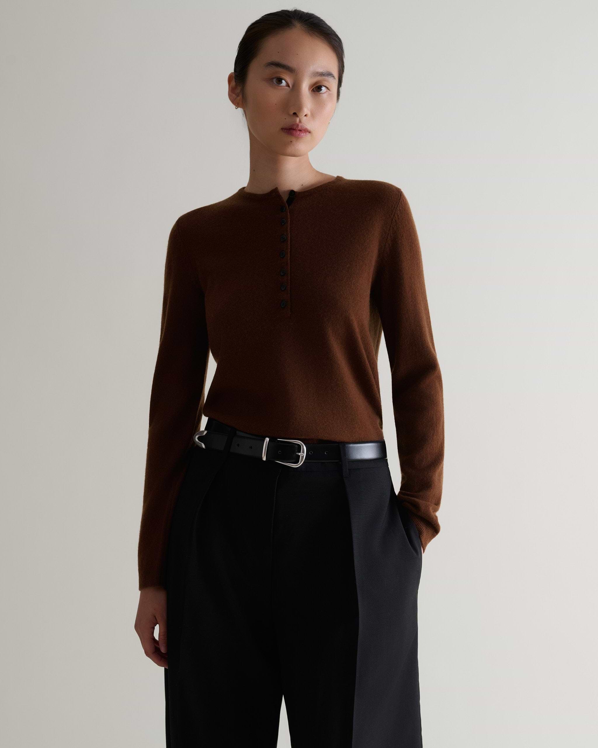Image 1 of 5 showing a woman wearing Rise & Fall's brown cashmere merino henley jumper with black trousers and a black belt.