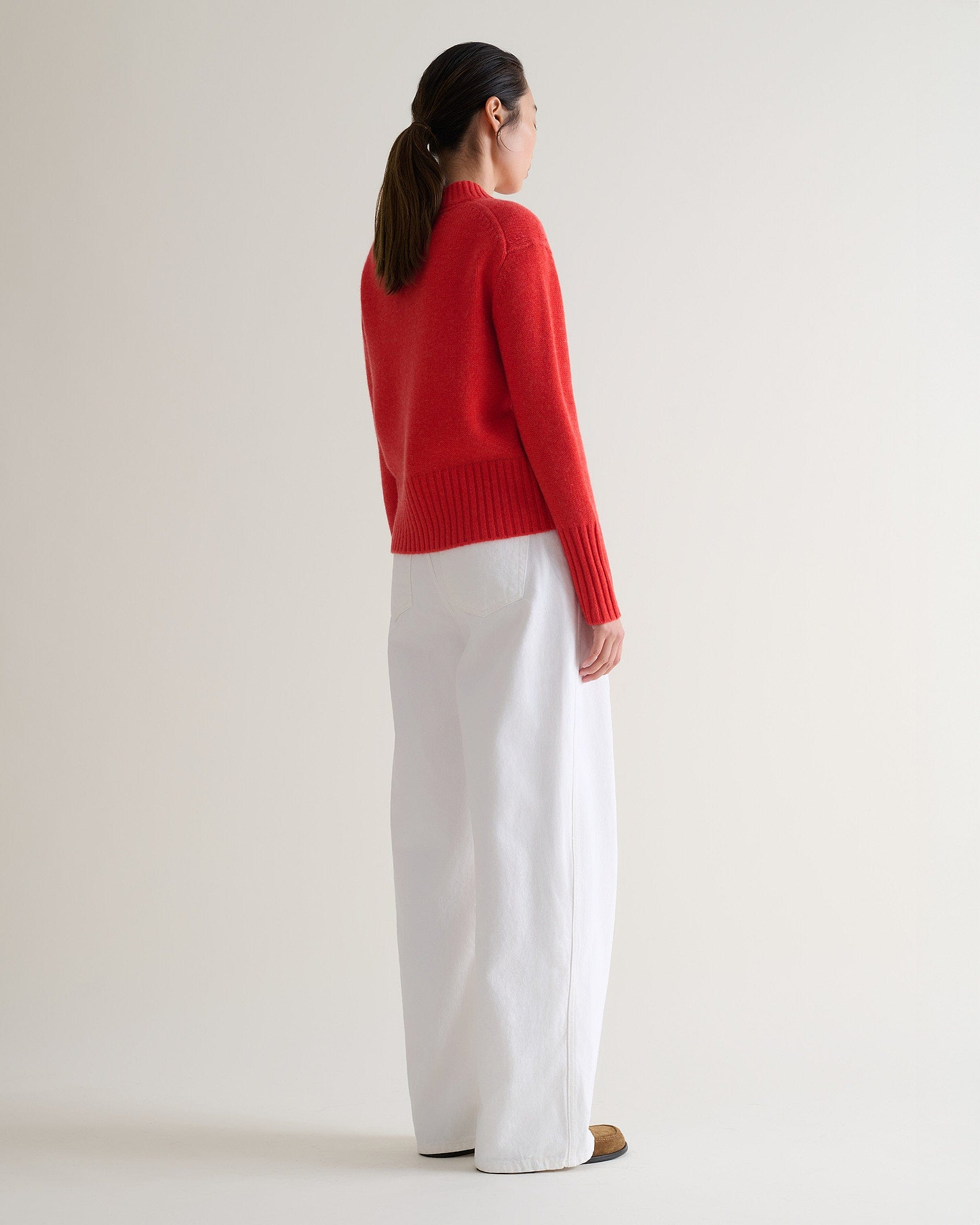Image 1 of 6 showing back of woman wearing Rise & Fall poppy red cashmere merino saddle sleeve crew neck jumper, with white wide leg jeans.