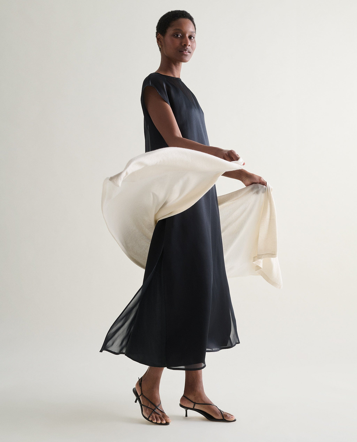 Image 2 of 6 showing woman wearing with Rise & Fall's oversized cashmere scarf in buttermilk with black-maxi-dress. 