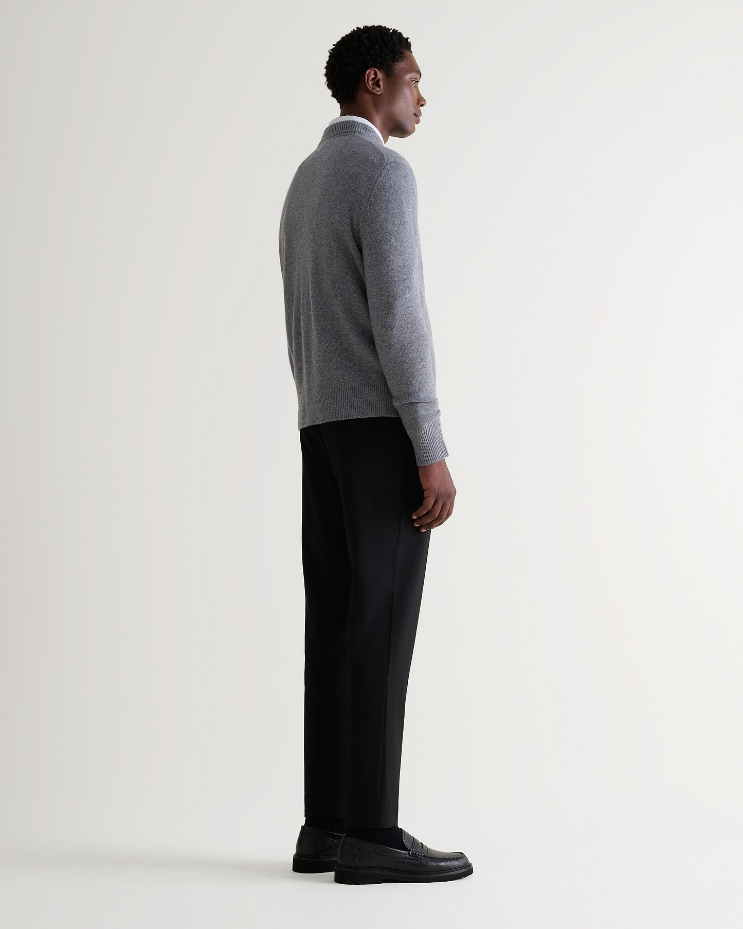 Image 3 of 5 showing side view of man wearing Rise & Fall's finest cashmere mid-weight crew neck jumper in grey with white shirt and black jeans.