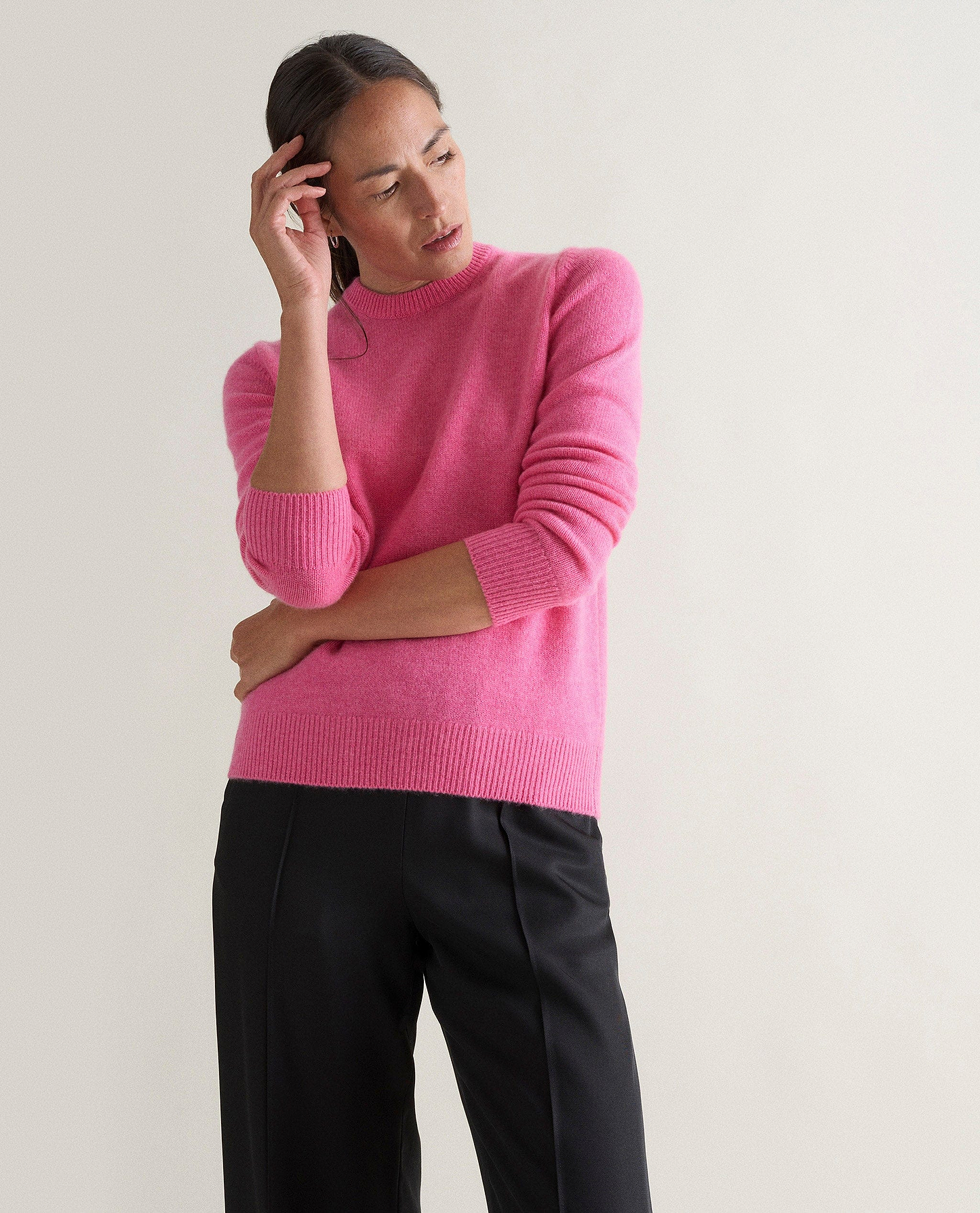 Image 3 of 5 showing woman wearing Rise & Fall's pink mid weight cashmere crew neck jumper with black trousers.