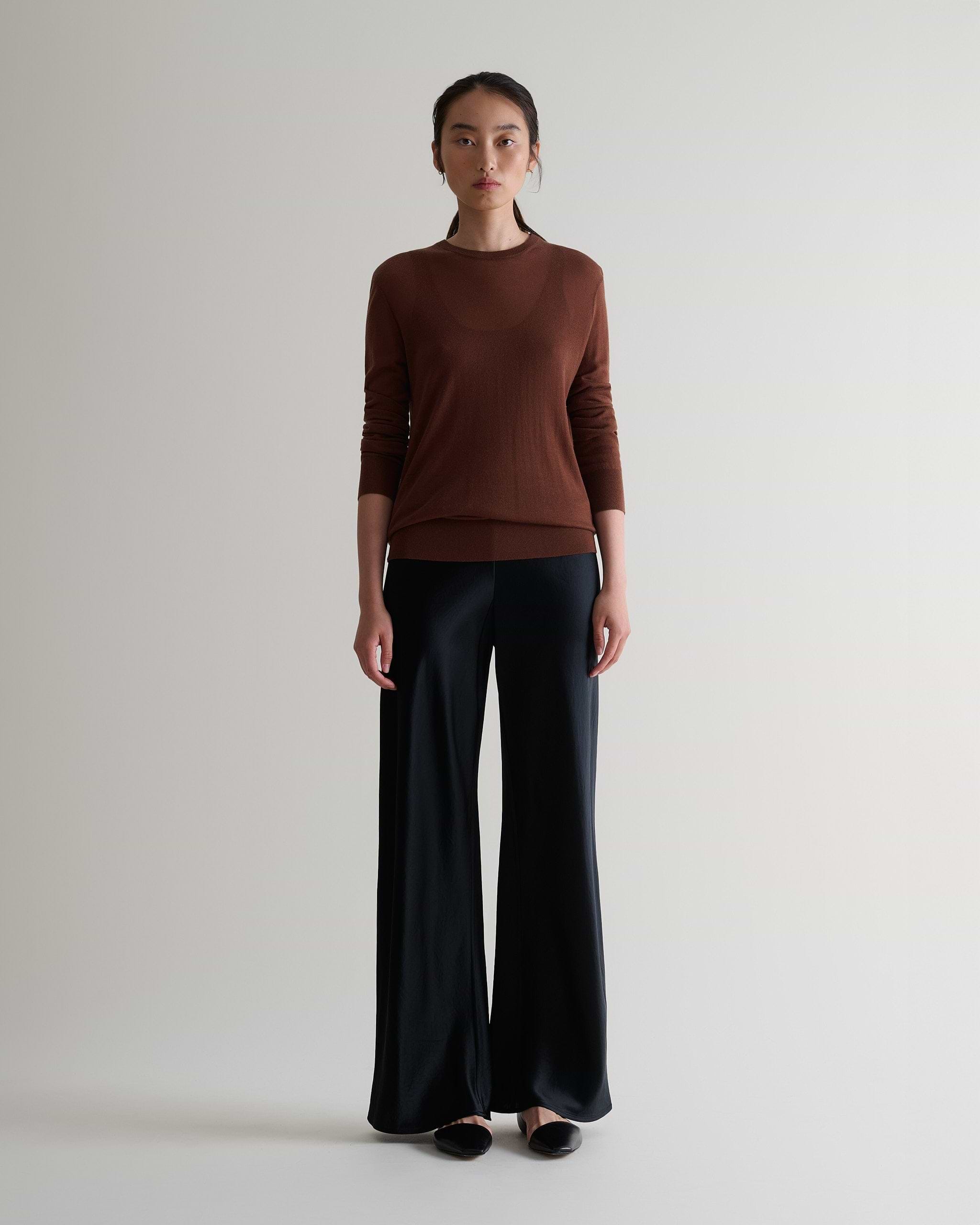 Image 3 of 6 showing woman wearing Rise & Fall's brown tencel cashmere double layered crew neck jumper with black trousers.