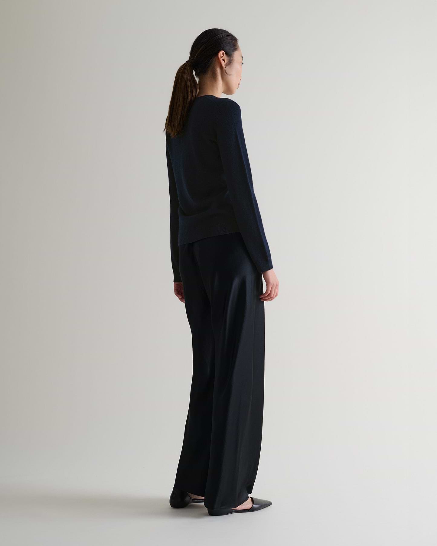 Image 3 of 6 showing side view of a woman wearing Rise & Fall's indigo cashmere merino henley jumper with black silk trousers.