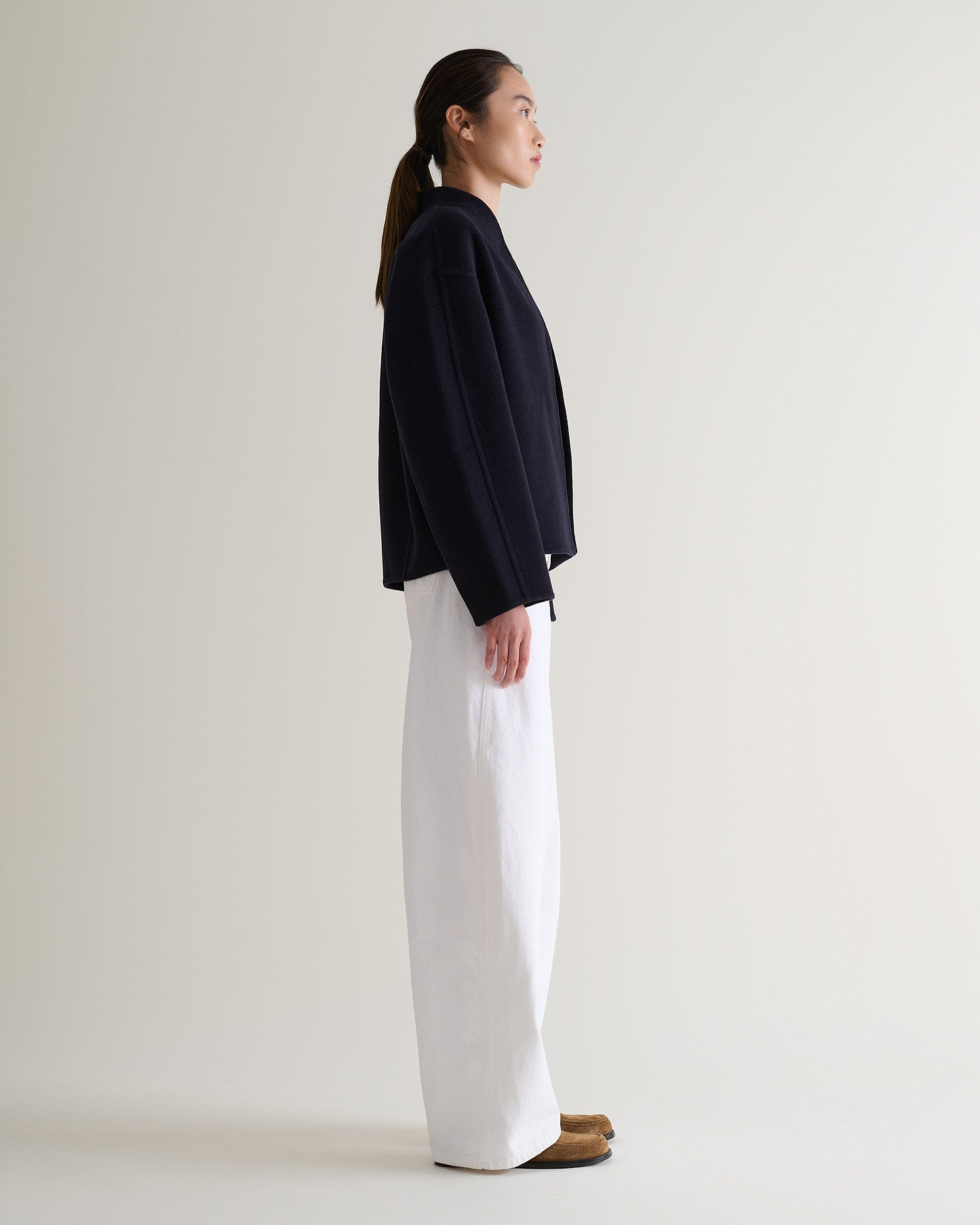 Image 3 of 7 showing side view of woman wearing Rise & Fall's navy cashmere wool double faced scarf jacket with white jeans.