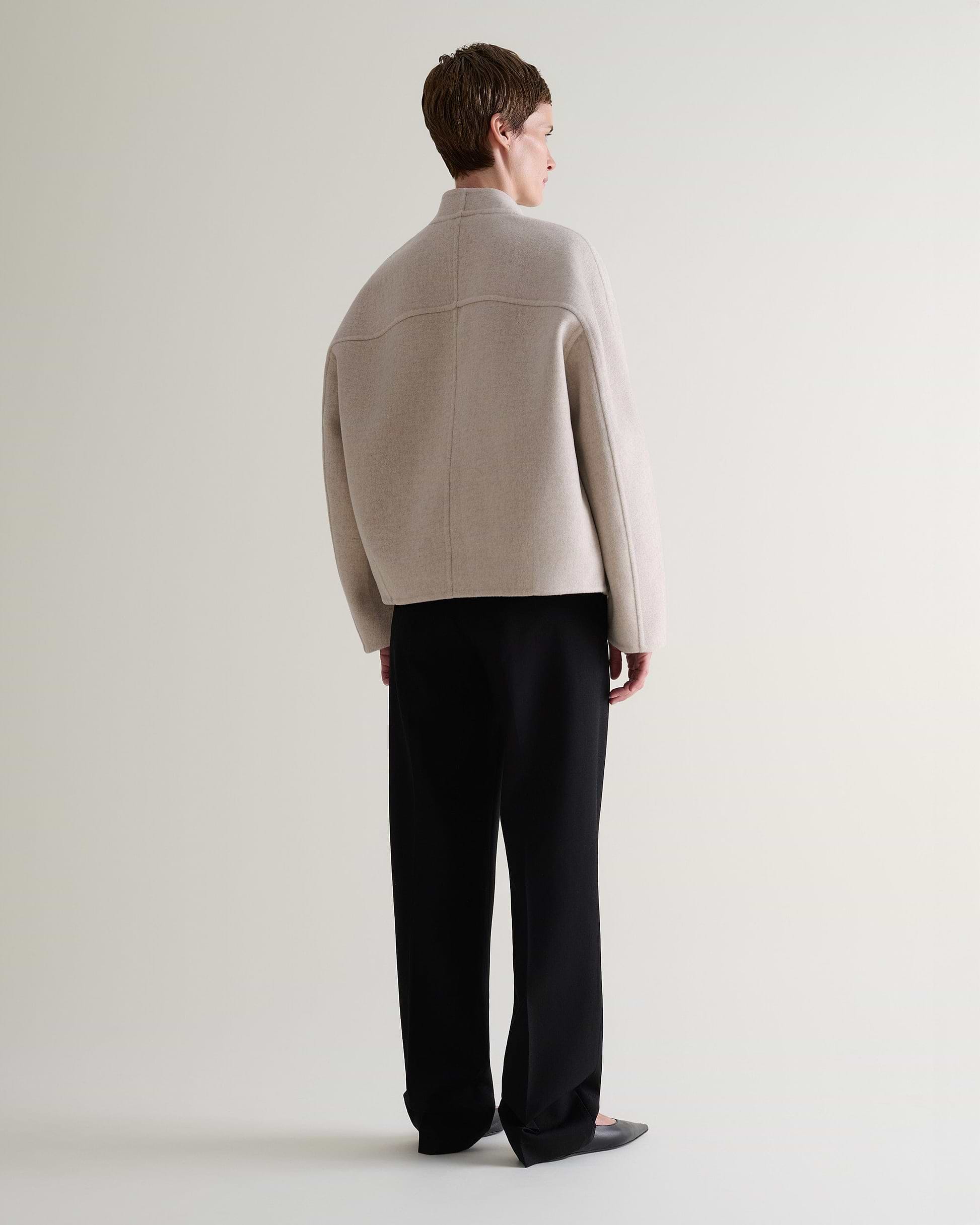 Image 3 of 9 showing back view of woman wearing Rise & Fall's twine cashmere wool double faced scarf jacket with black trousers.