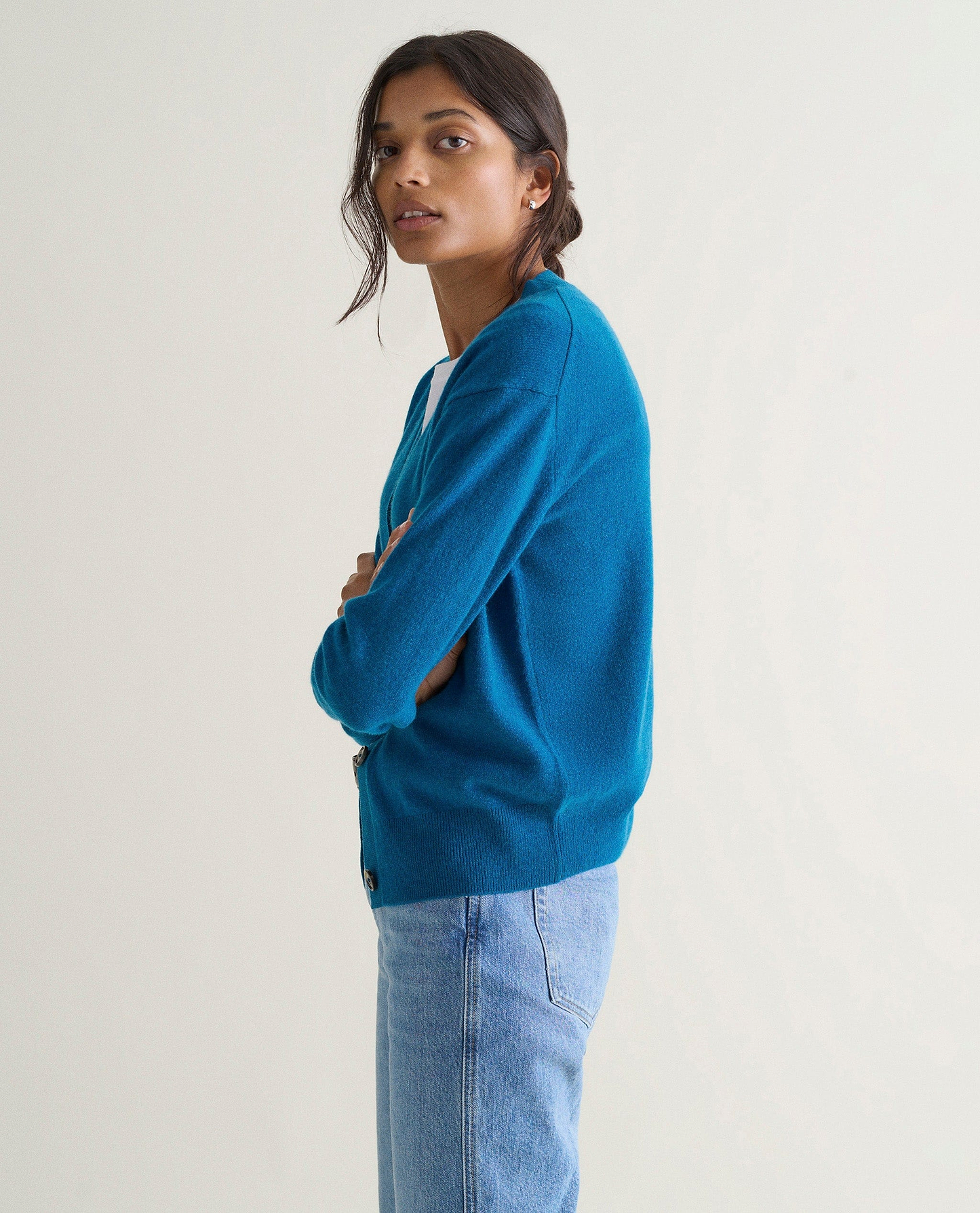 Image 4 of 5 showing side view of a woman wearing Rise & Fall's viridian blue fine cashmere v-neck cardigan with a pair of jeans.