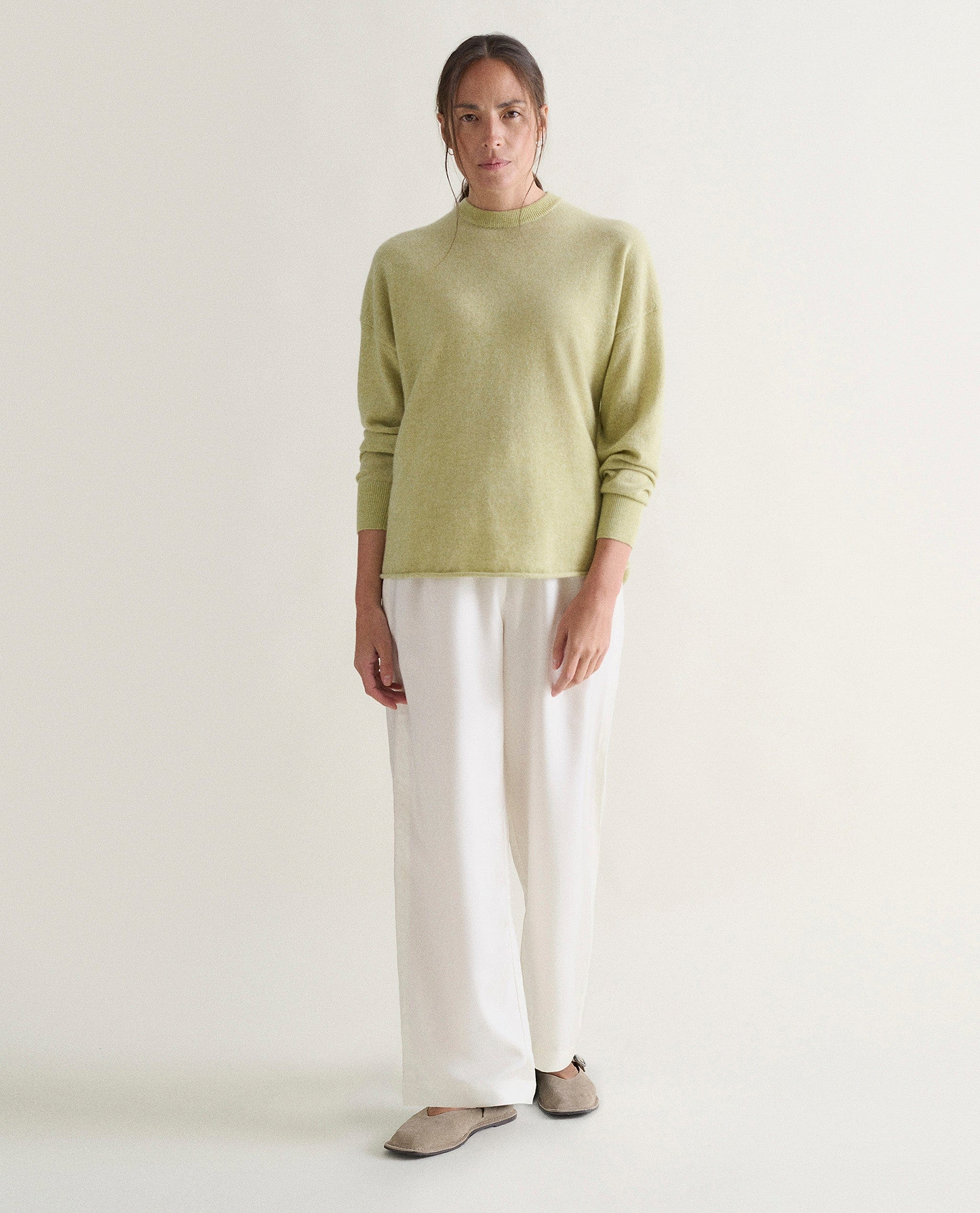 Image 4 of 5 showing woman wearing Rise & Fall's lichen green fine cashmere sweatshirt with white trousers.