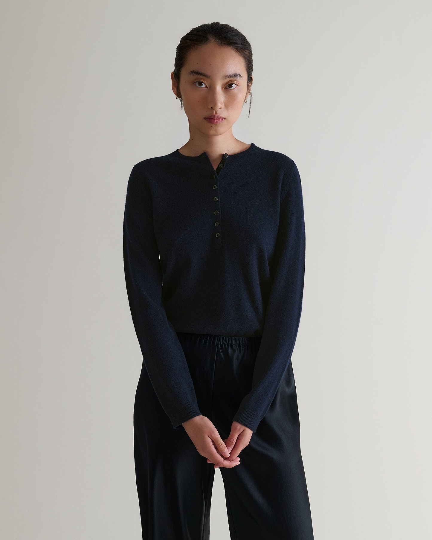 Image 4 of 6 showing a woman wearing Rise & Fall's indigo cashmere merino henley jumper with black silk trousers. 