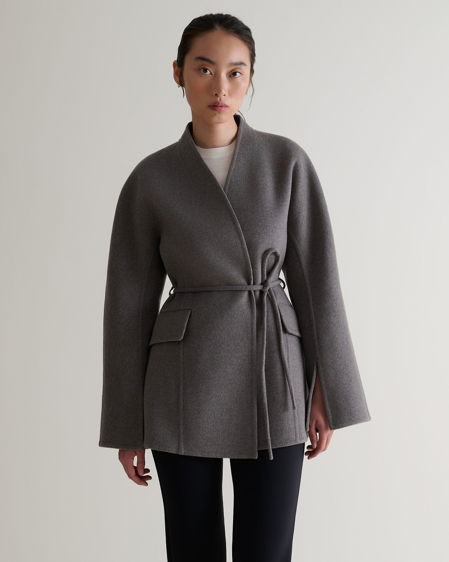 Image 4 of 7 showing woman wearing Rise & Fall's fawn cashmere wool double faced sculptural jacket with white t-shirt and black trousers.