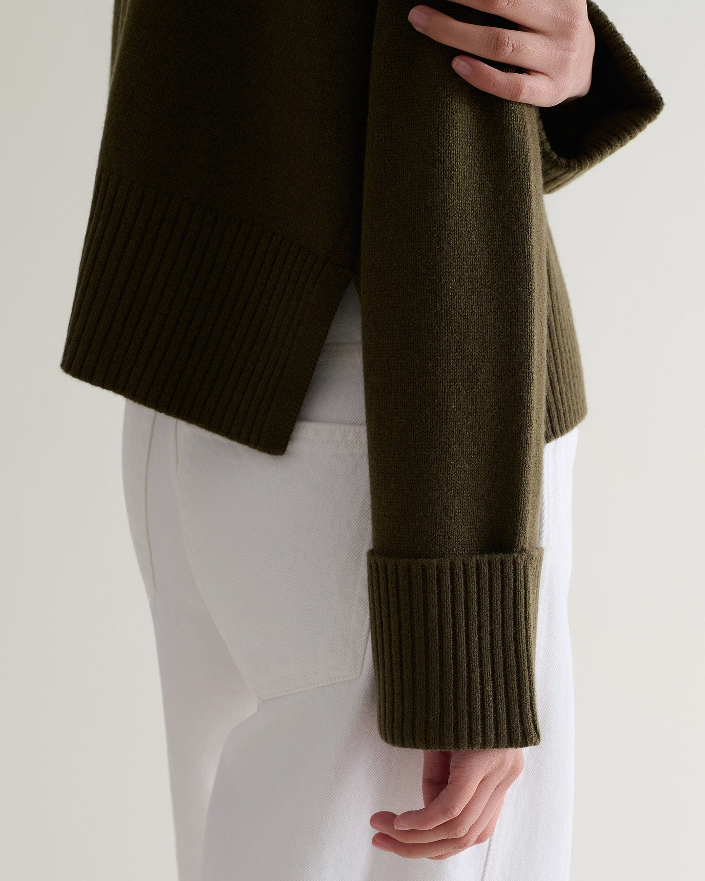 Image 5 of 5 showing close up side view of Rise & Fall's military green cashmere merino high neck jumper with white jeans. 