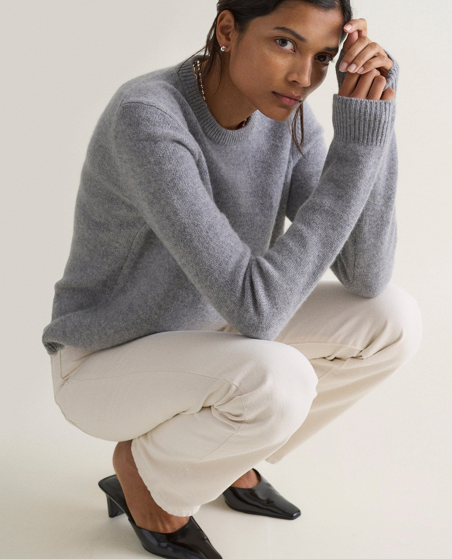 Image 5 of 5 showing a woman croutching wearing Rise & Fall's grey mid-weight cashmere crew neck jumper and white jeans.