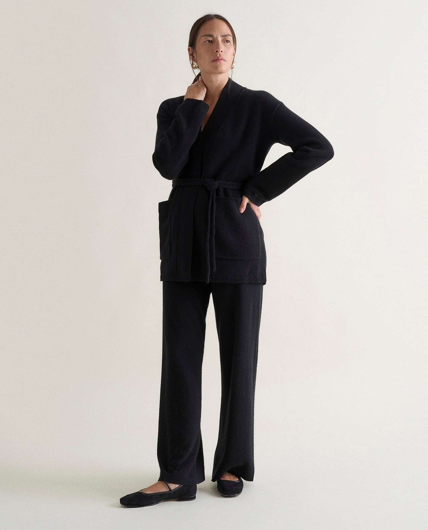 Image 5 of 5 showing woman wearing Rise & Fall's black cashmere merino belted cardigan with black trousers.