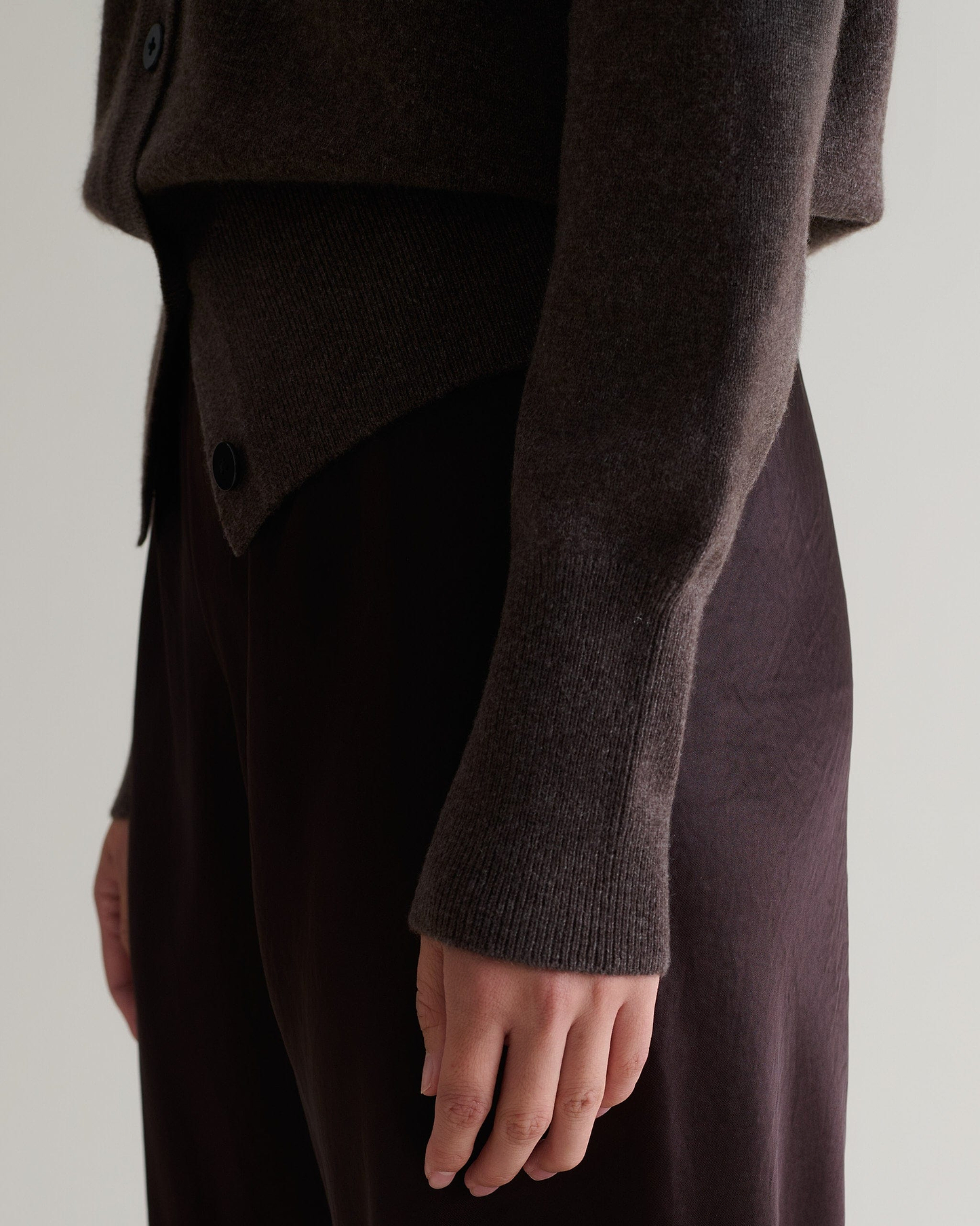 Image 5 of 6 showing close side view of Rise & Fall's chocolate fine cashmere blouson cardigan with silk brown trousers.
