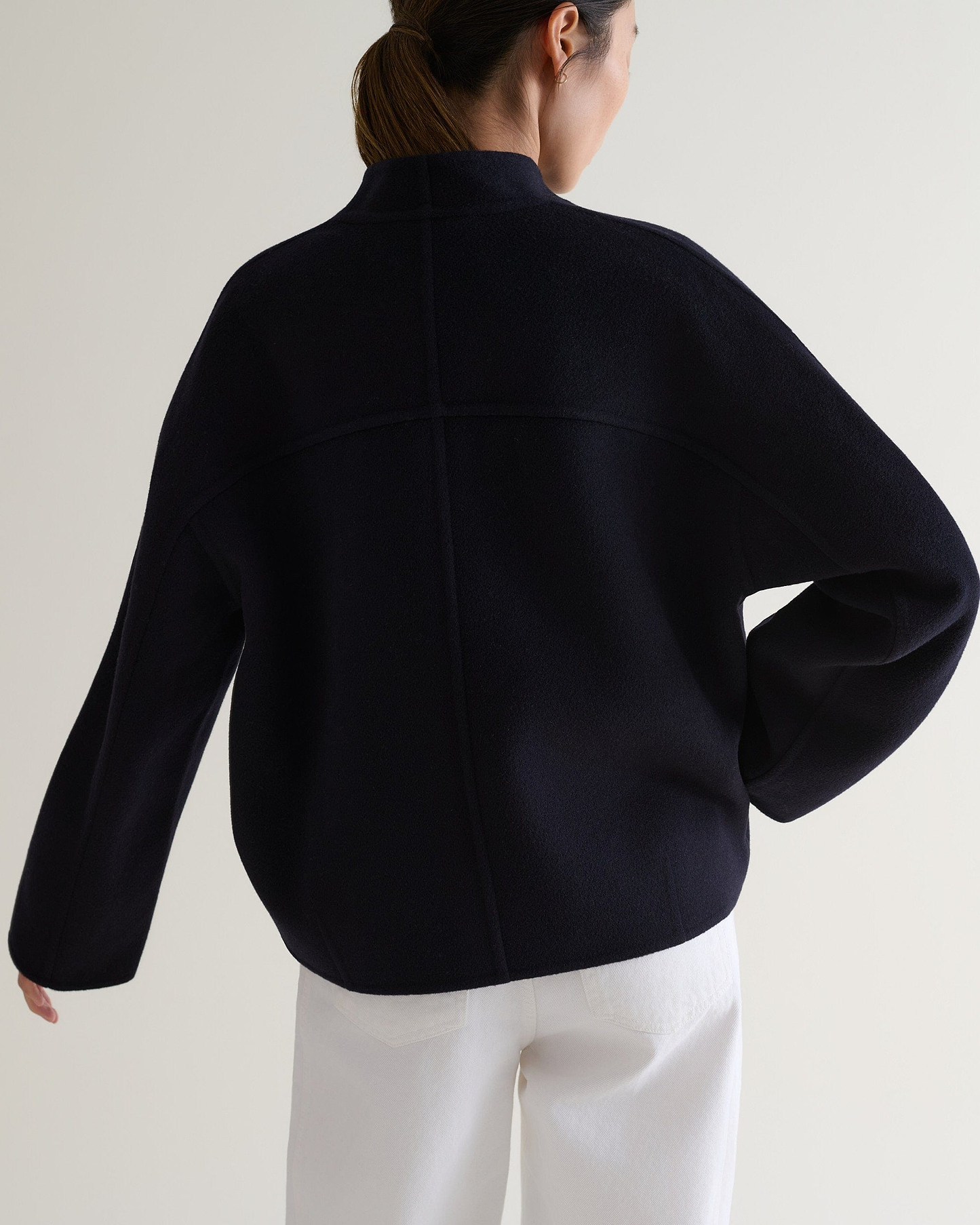 Image 5 of 7 showing back view of woman wearing Rise & Fall's navy cashmere wool double faced scarf jacket with white jeans.