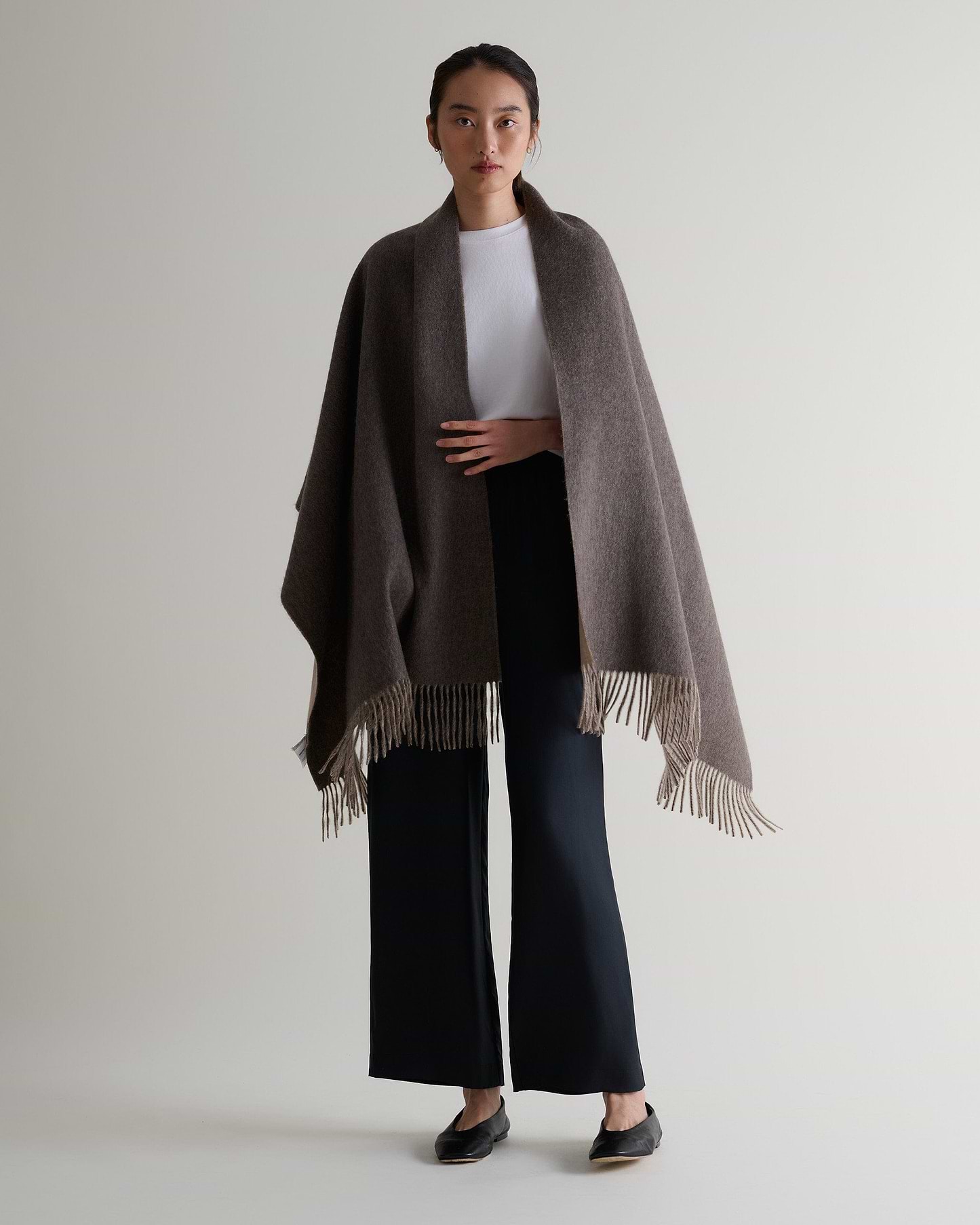 Image 6 of 7 showing woman wearing Rise & Fall's finest cashmere double faced wrap mole side with white T-shirt and black trousers.