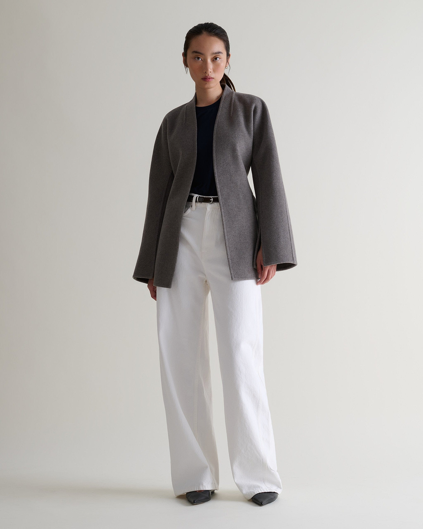 Image 7 of 7 showing woman wearing Rise & Fall's fawn cashmere wool double faced sculptural jacket with black t-shirt and white jeans.