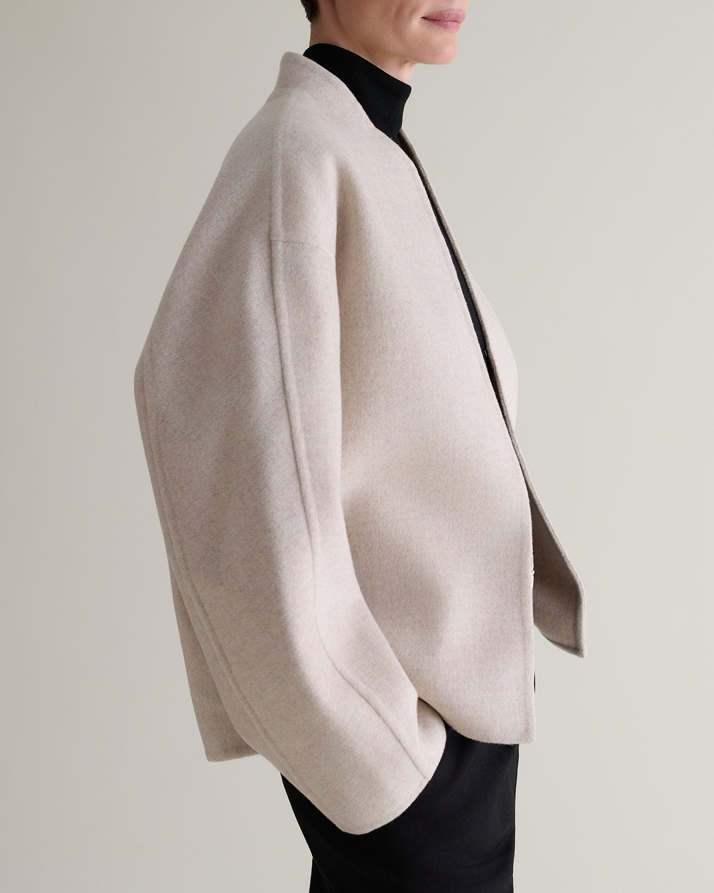 Image 7 of 9 showing side view of woman wearing Rise & Fall's twine cashmere wool double faced scarf jacket with black trousers and roll neck jumper.