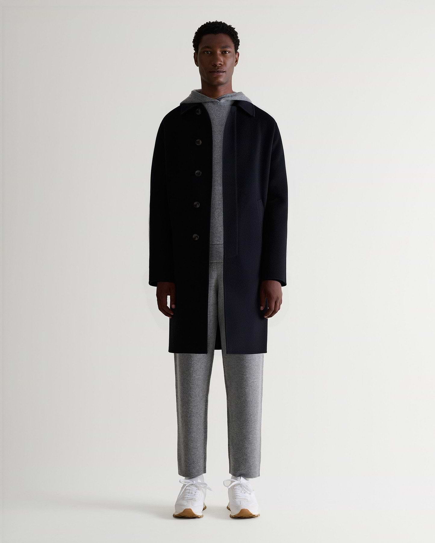 Full front view of man wearing Rise & Fall's grey cashmere merino double-faced hoodie and joggers with black wool coat.