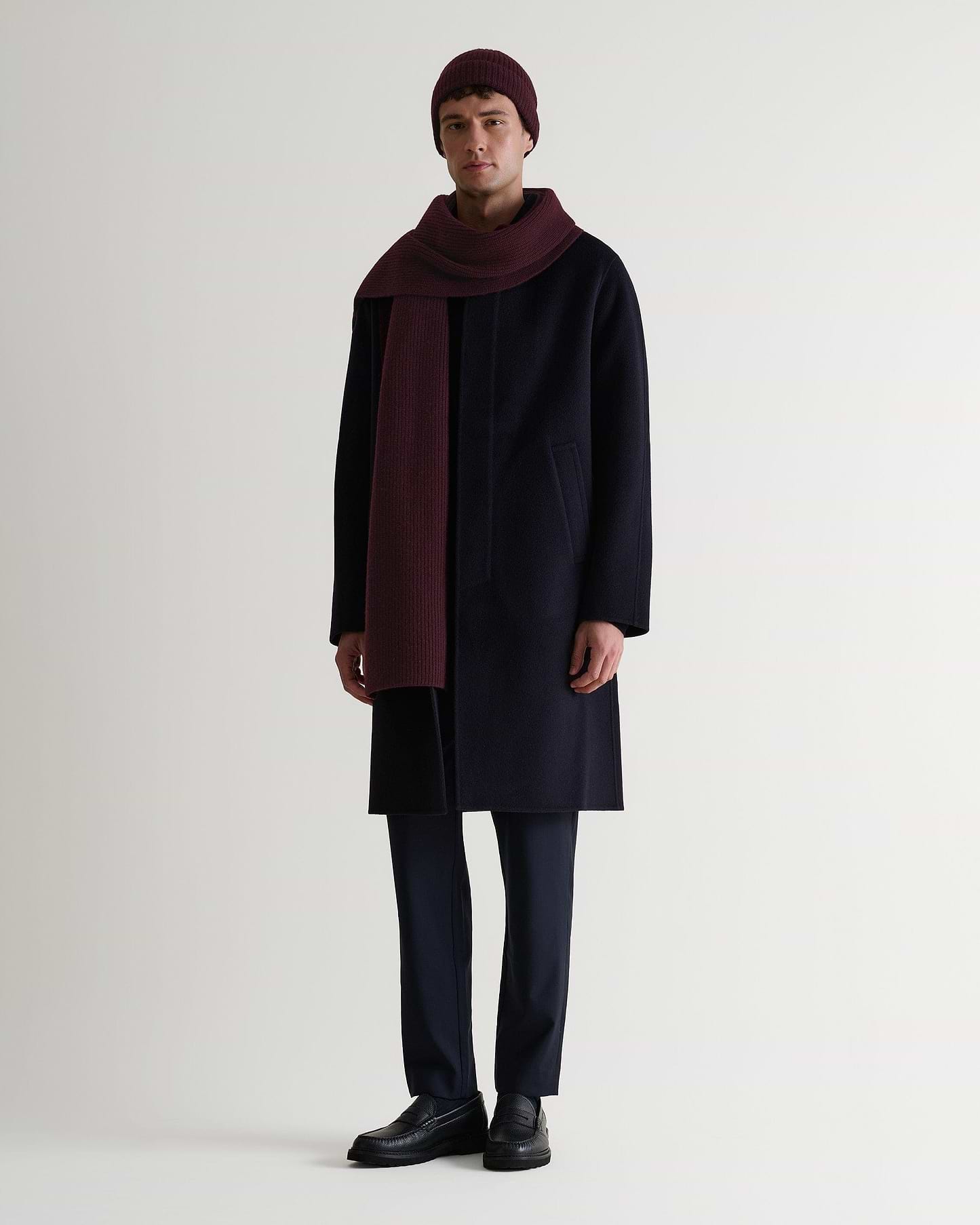 Full portrait view of man wearing Rise & Fall's oxblood cashmere merino ribbed scarf with matching coloured beanie and navy wool coat