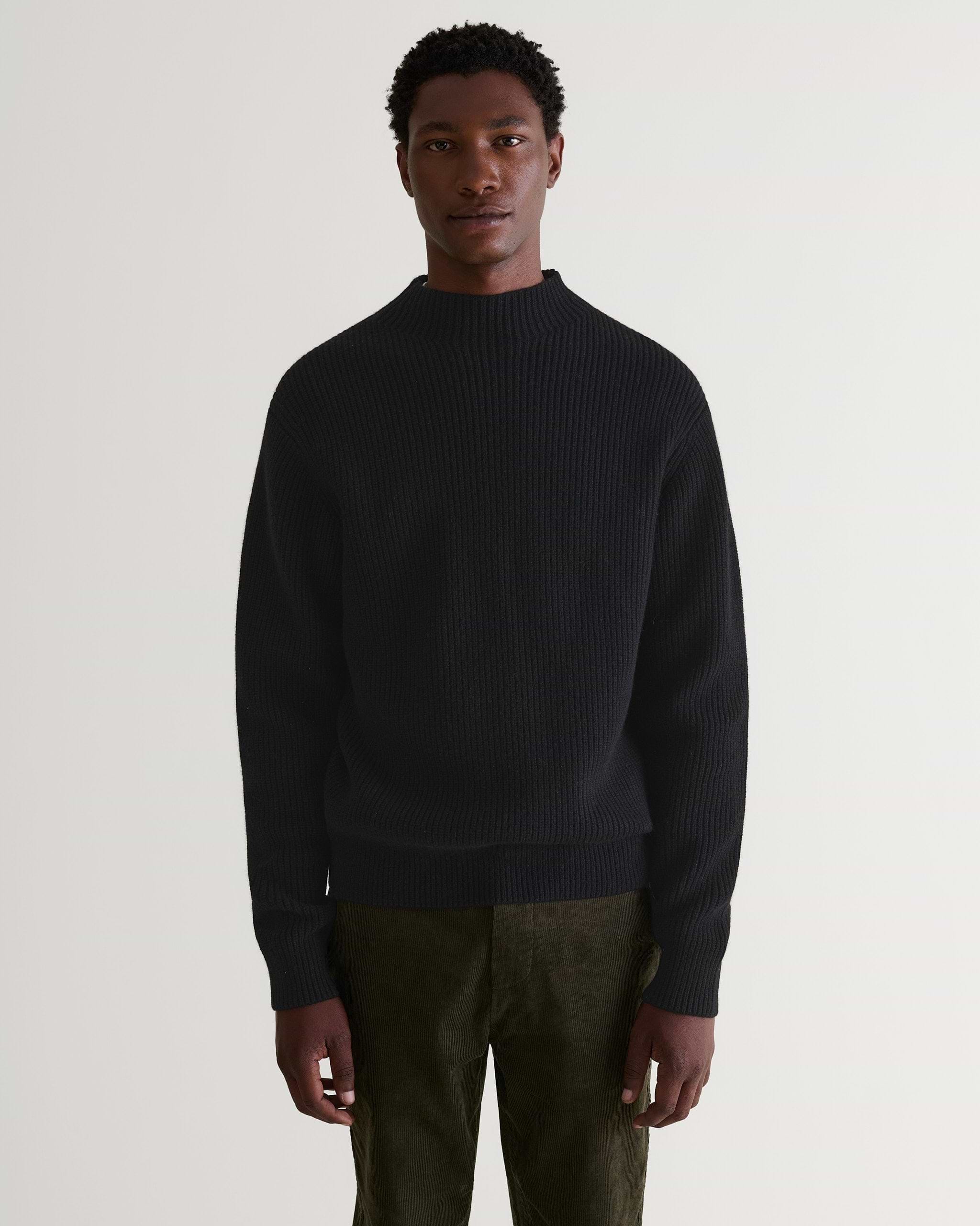 Front view of man wearing Rise & Fall's black cashmere merino stand neck ribbed sweater with dark green corduroy trousers.
