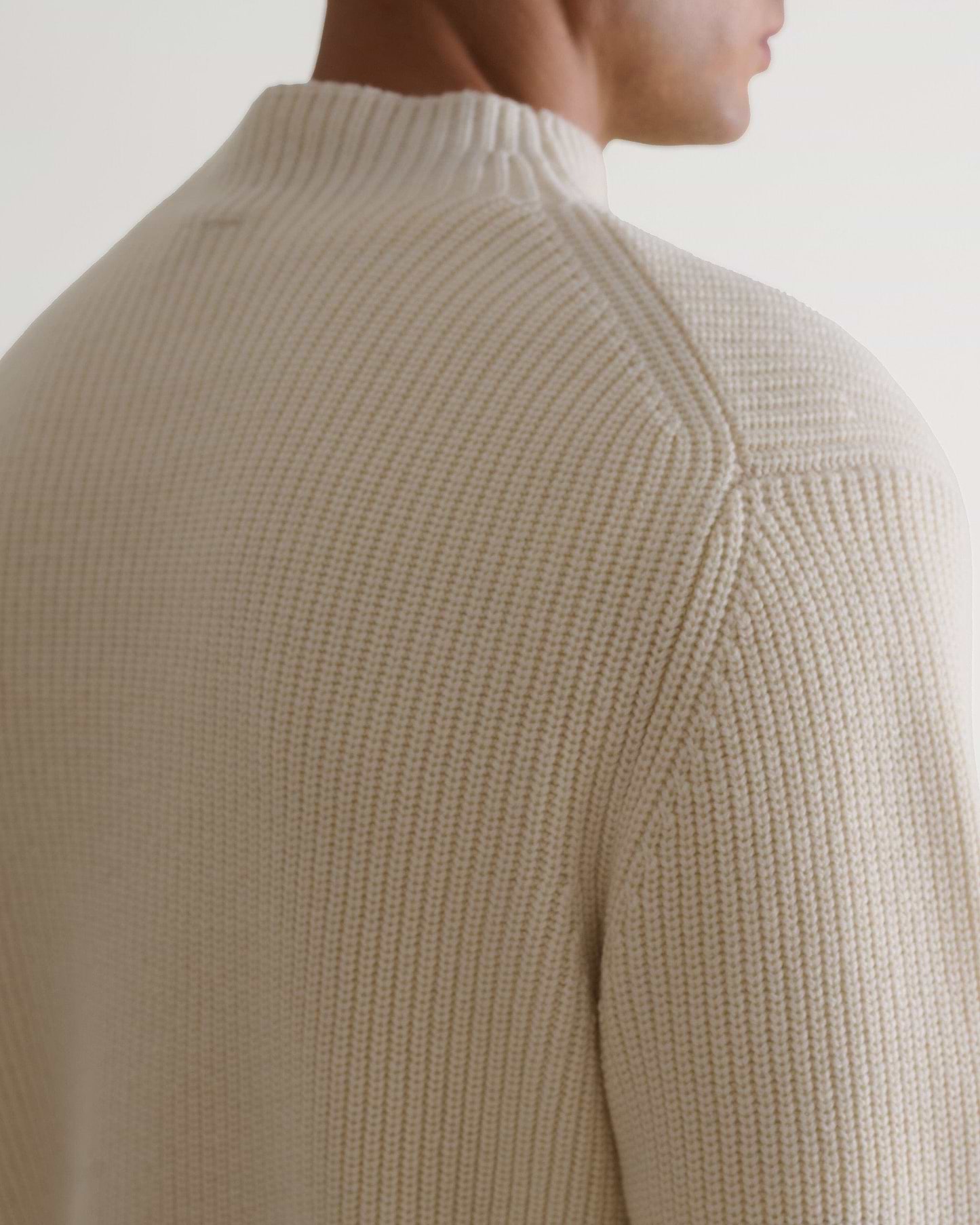Man wears Rise & Fall's cream cashmere merino stand neck jumper. A close up of shoulder.