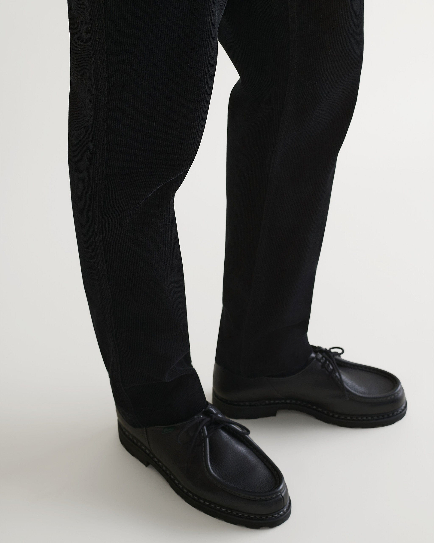 Close up of Rise & Fall's black corduroy trousers with black leather shoes.